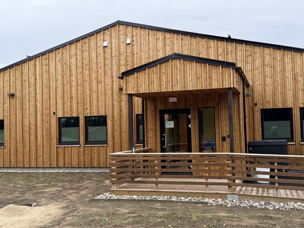 Barnahus i trä med fasad i naturträ och takförsedd entré.tré