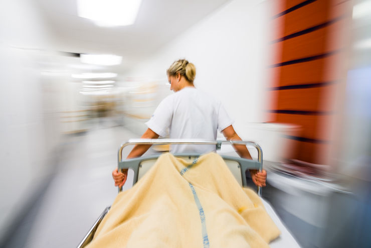Vårdanställd drar sjukhussäng i korridor.