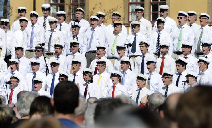 Singing men outdoors wearing student caps.