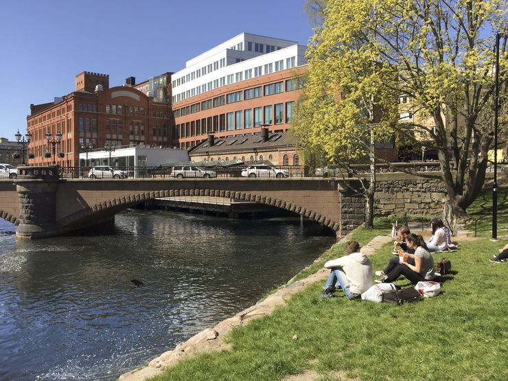 Människor sitter på en gräsmatta, i bakgrunden syns campus Norrköping