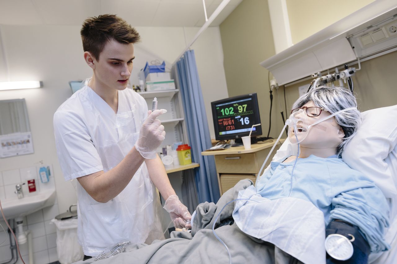 Nurse student trains care on doll lying in bed.