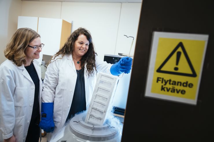 two female researchers by a cryo tank in a lab.