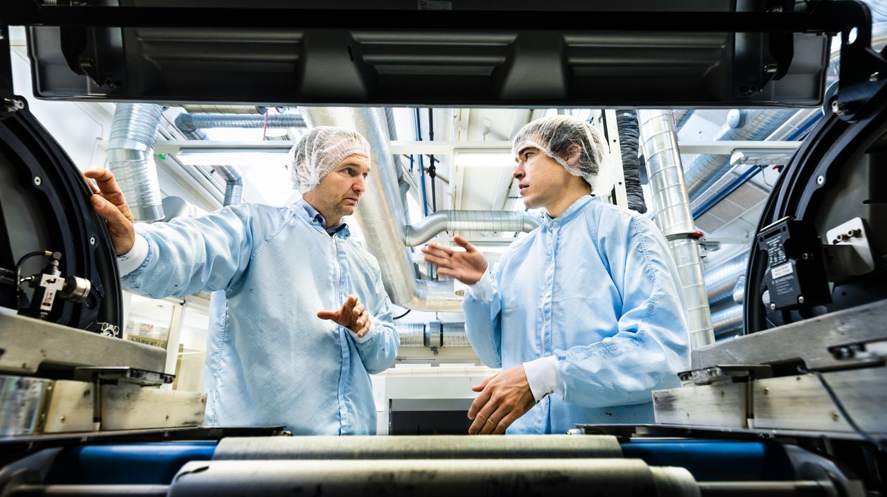 Two men wearing protective gear are talking to each other. The picture is taken through a machine which works as a frame.