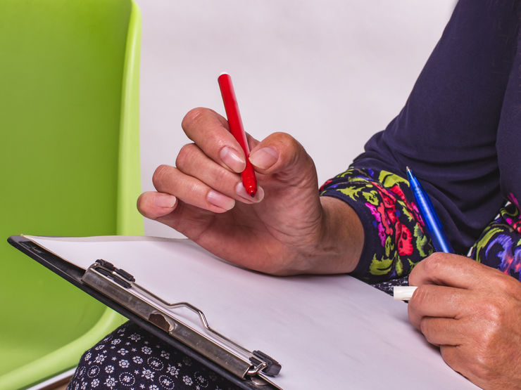 Adult woman in pattern dress with red felt pen writing in a notebook.