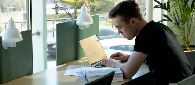 A male student with a laptop and a book.