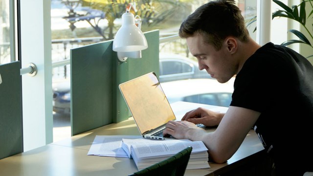 A male student with a laptop and a book.