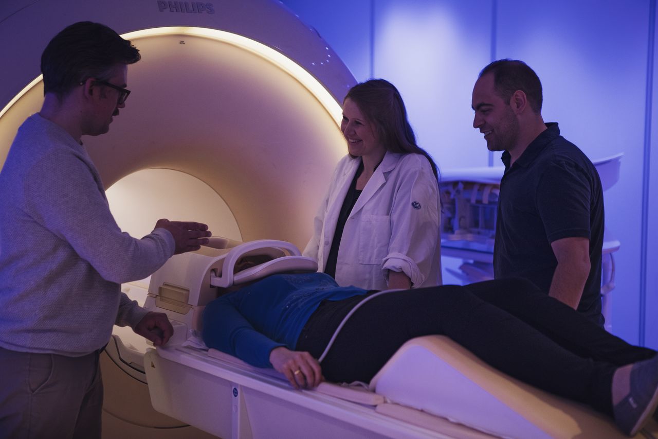 Three researchers are standing around a patient in an MRI.