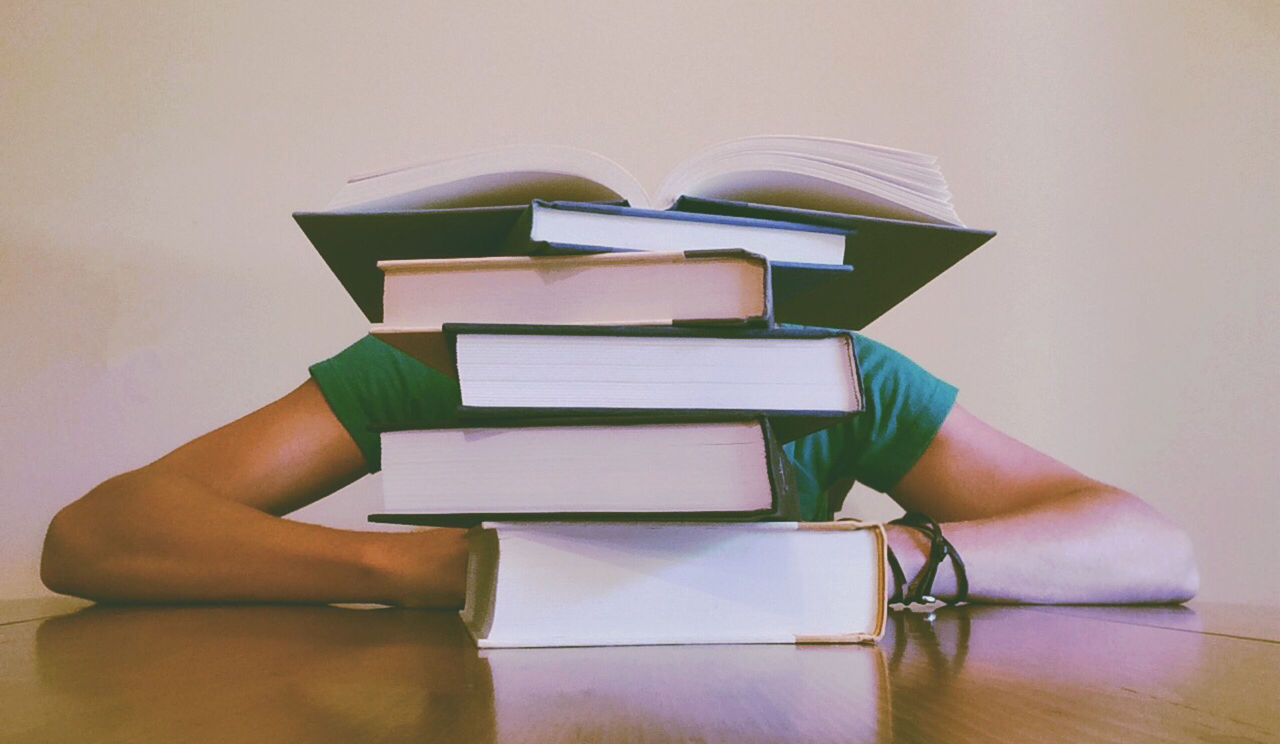 A pile of books on a table in front of a person.