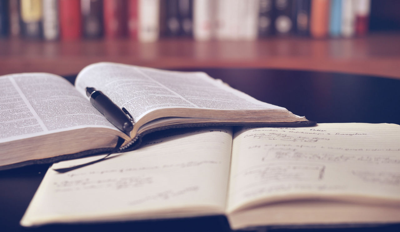 An open book with a pen in it, on top of a notebook.