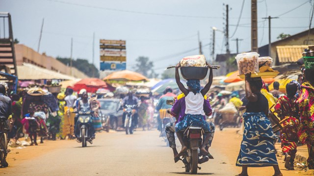 Bohicon, Benin - September 8, 2012: People crossing the street in busiest market junction in town, lot of motorbikes in background.