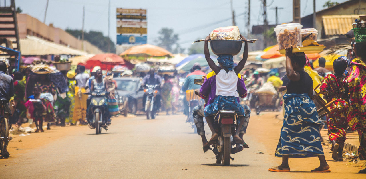 Bohicon, Benin - September 8, 2012: People crossing the street in busiest market junction in town, lot of motorbikes in background.