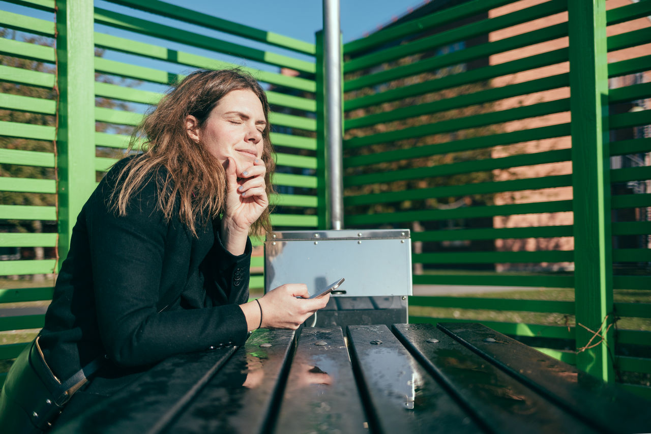 En kvinna sitter och i universitetsparken på Campus Valla, Linköpings universitet.