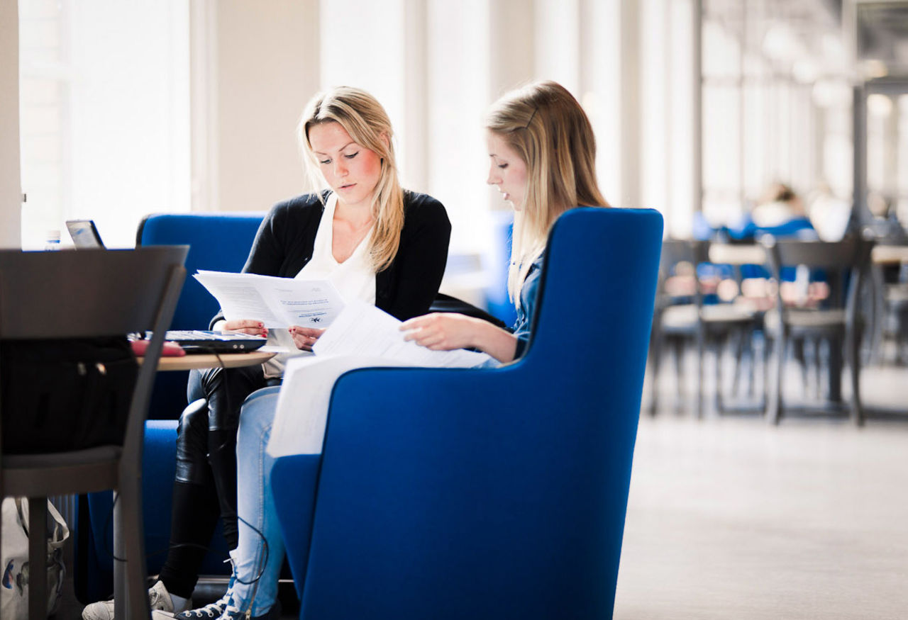Två kvinnliga studenter sitter i fåtöljer och läser