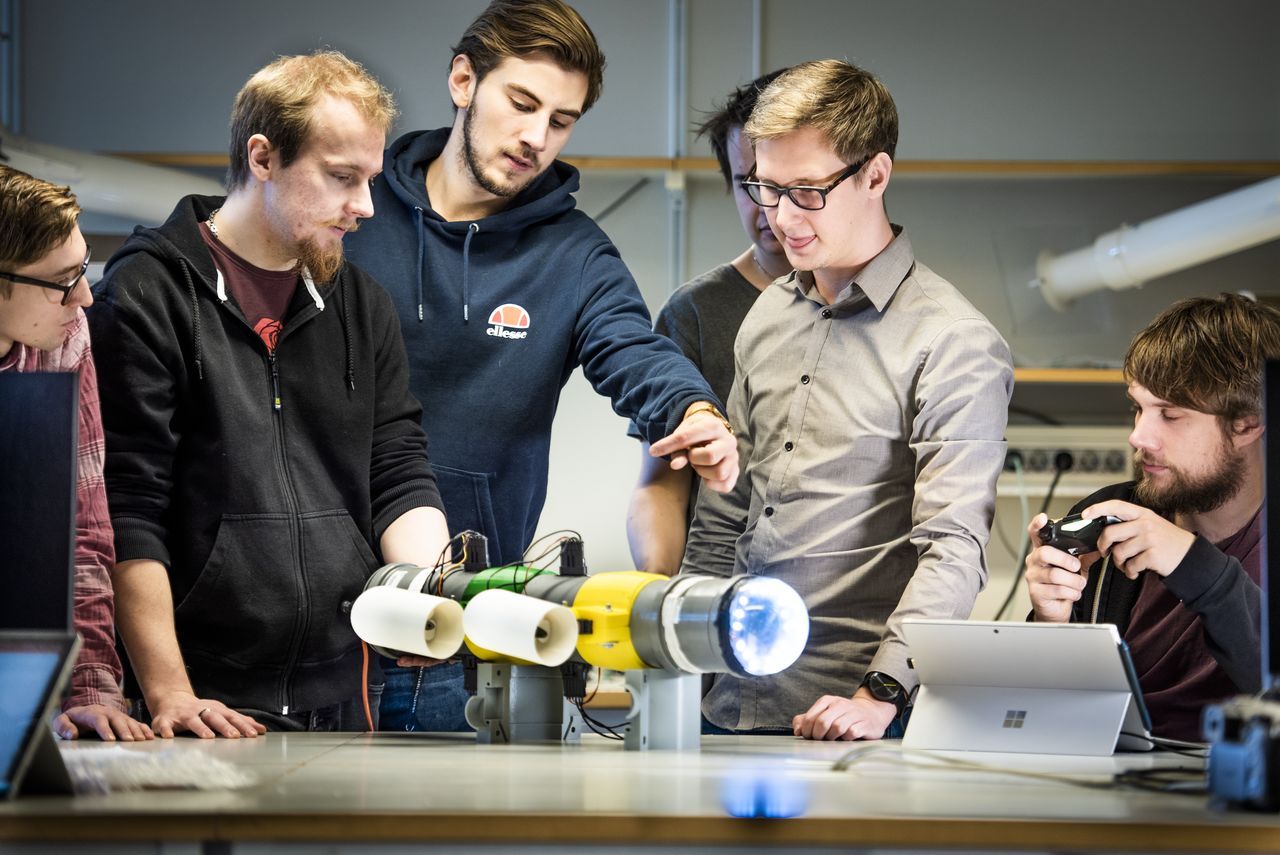 Six student standing around a table watching a robot they built