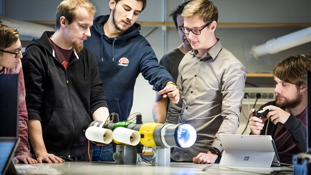Sex studenter står runt ett bord och tittar på en robot de byggt