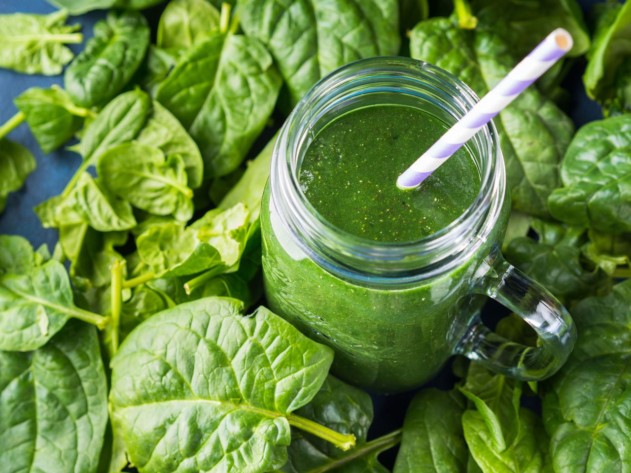 Green spinach spirulina smoothie in mason jar on blue background