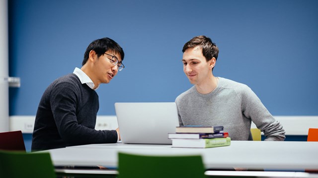 Two PhD students discuss at a computer