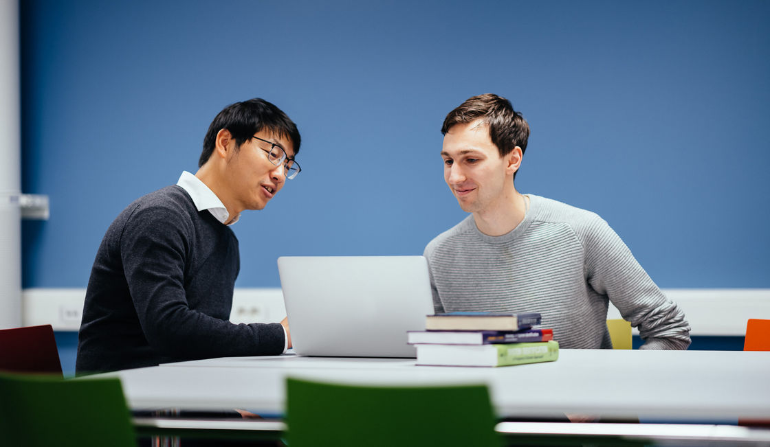 Two PhD students discuss at a computer