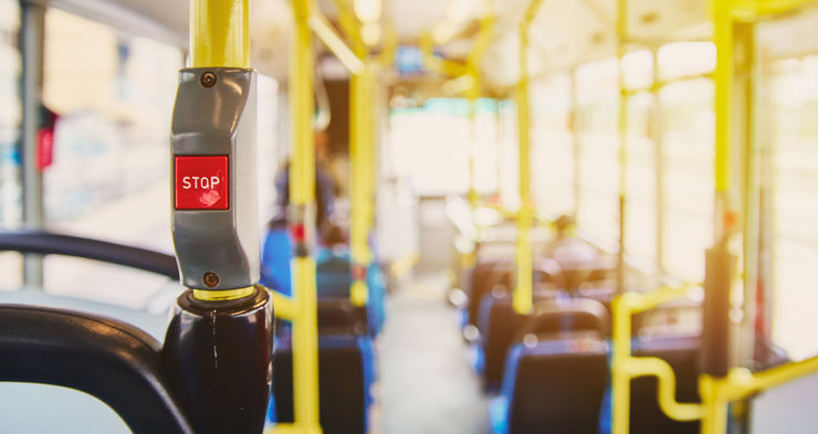 Red button STOP on the bus. Bus with yellow handrails and blue seats. Photo with the sun effect, glare on the lens from the light. Spacious interior of the bus, bright button with focus