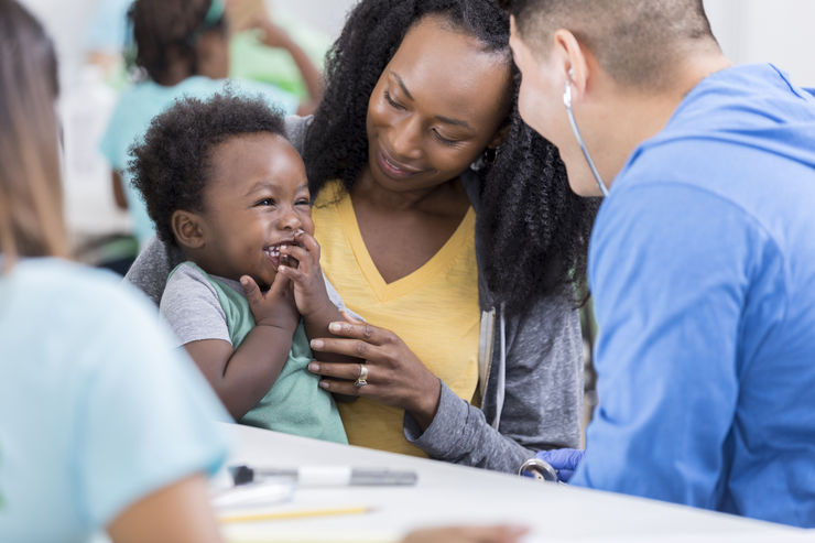 Caring male doctor smiles while talking to a baby boy in a free clinic. The boy's mom is holding him.