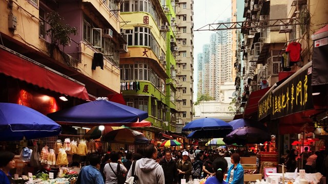 The image shows people at a food market set among tall buildings