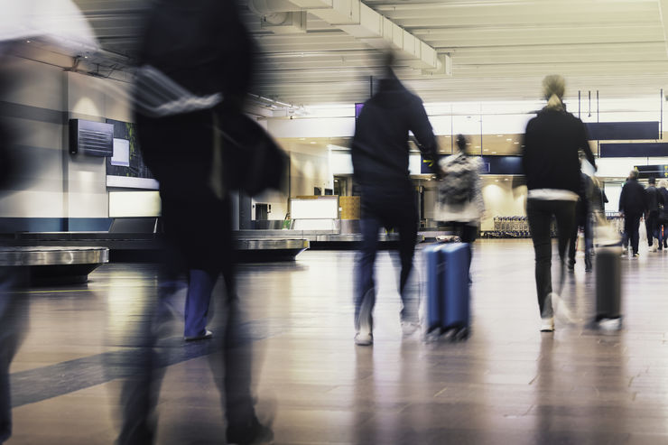 People in motion walking with luggage through an airport walkway.