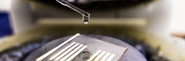 Closeup of a pipette dripping a clear fluid on to a microscope