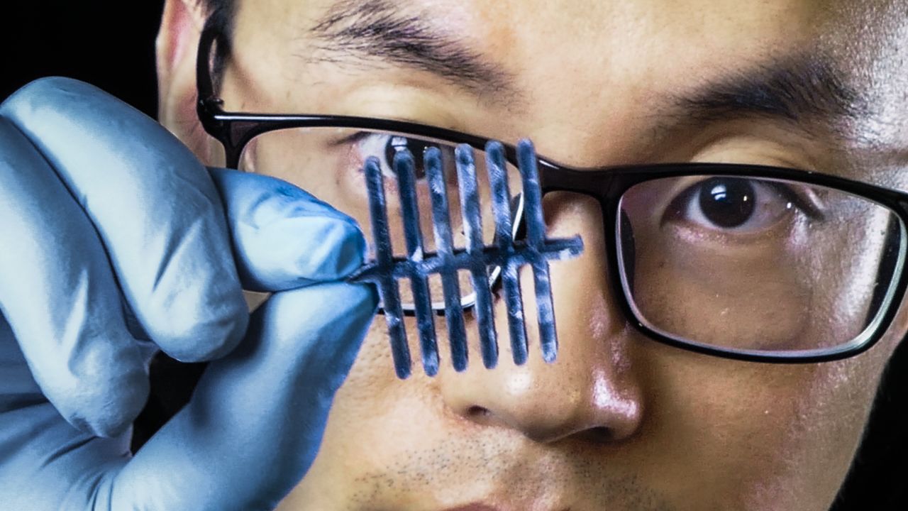 Closeup on a man who is holding a sensor in front of one of his eyes. He is wearing a blue rubber glove.