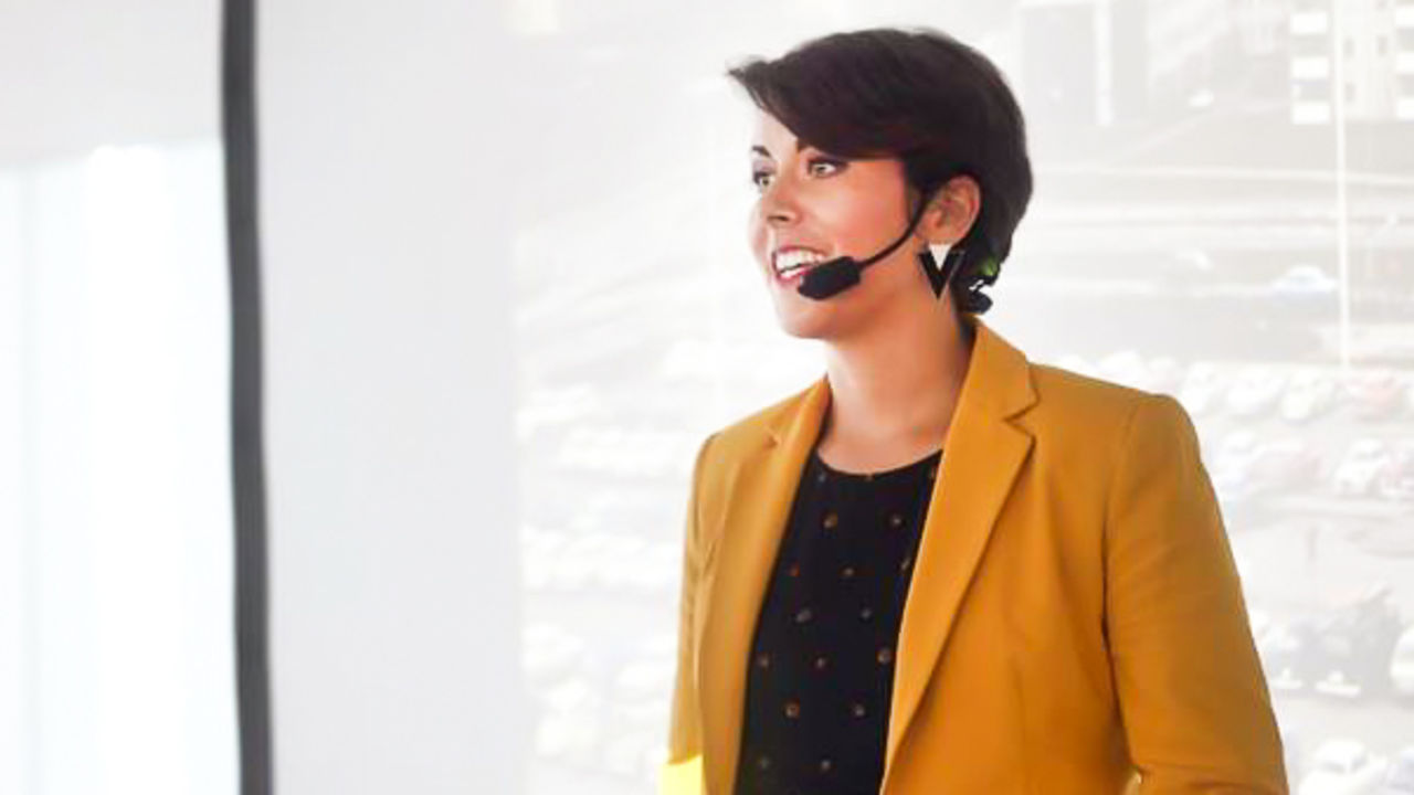 Kvinna i gul kavaj med kortklippt hår talar i headset