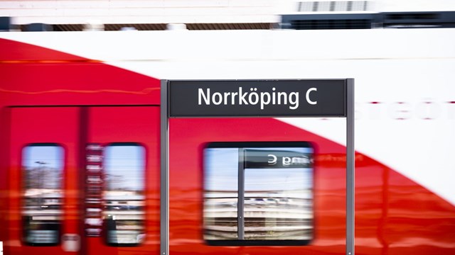På en skylt står det "Norrköping C" i bakgrunden åker ett tåg förbi.