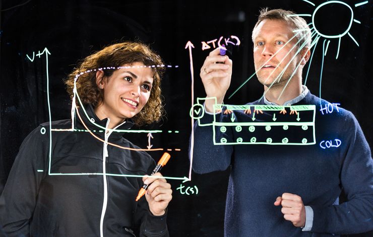 Mina Shiran Chaharsoughi and Magnus Jonsson photographed through a sheet of glass on which they are writing formulas.