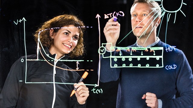 Mina Shiran Chaharsoughi and Magnus Jonsson photographed through a sheet of glass on which they are writing formulas.