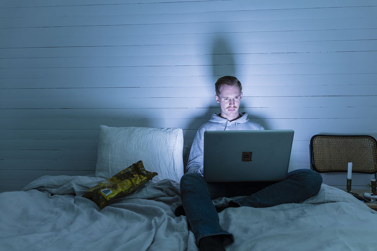 Man sits on a bed with laptop