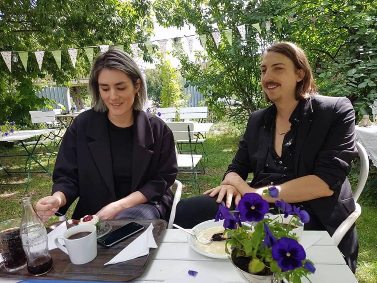 Two people eating cake in a garden.