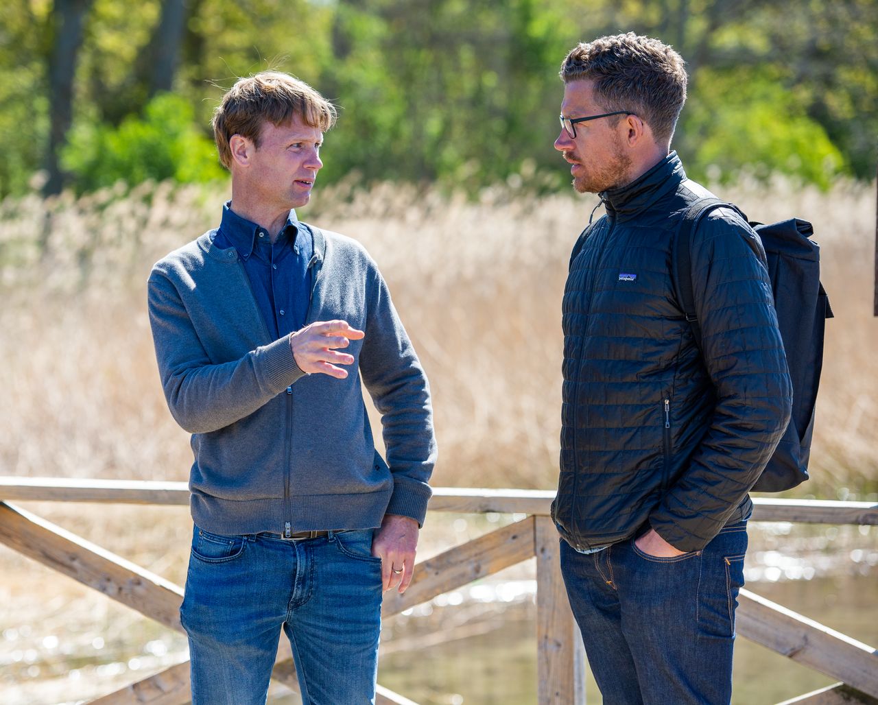 Två män står och samtalar i utomhusmiljö.