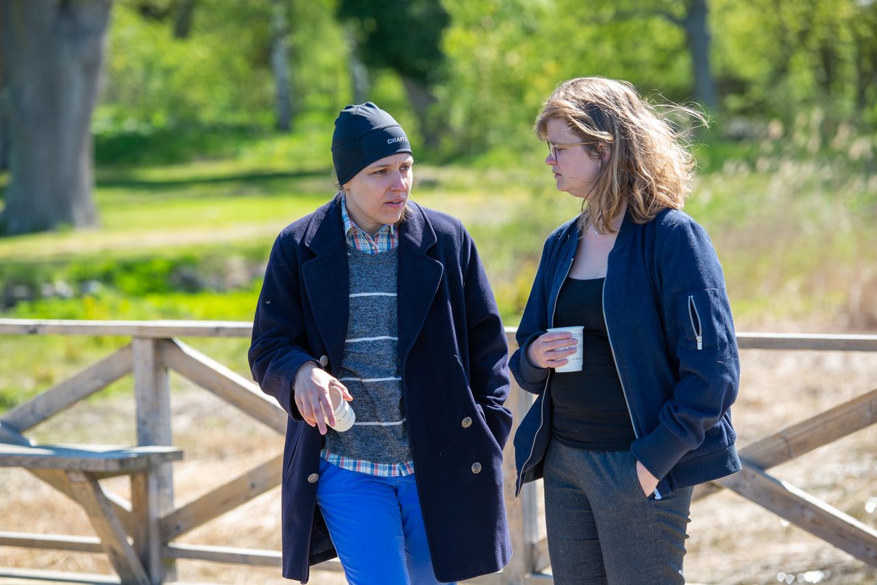 Två kvinnor står och samtalar i utomhusmiljö.