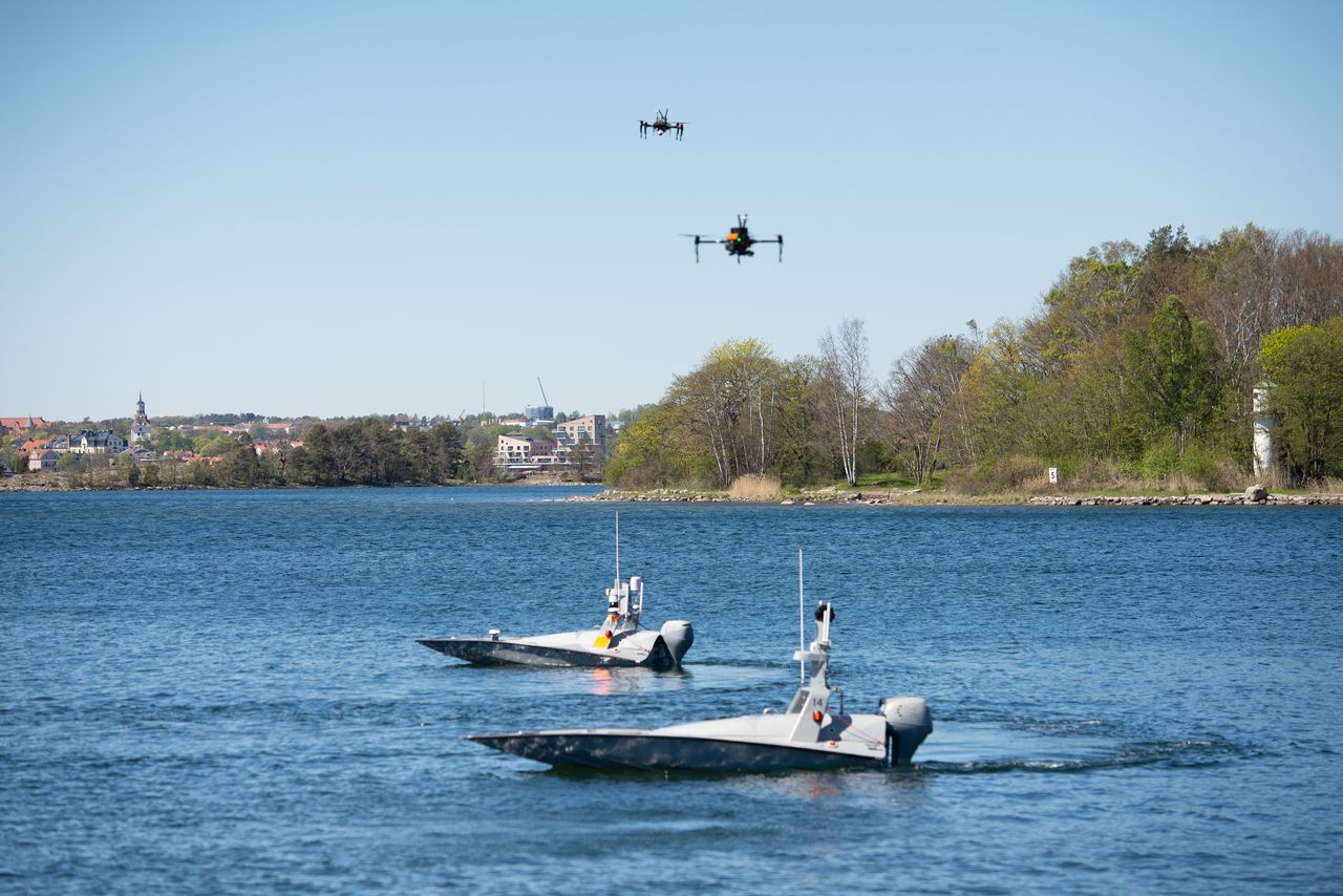 Two boats in the water and above them in the air two quadcopters.