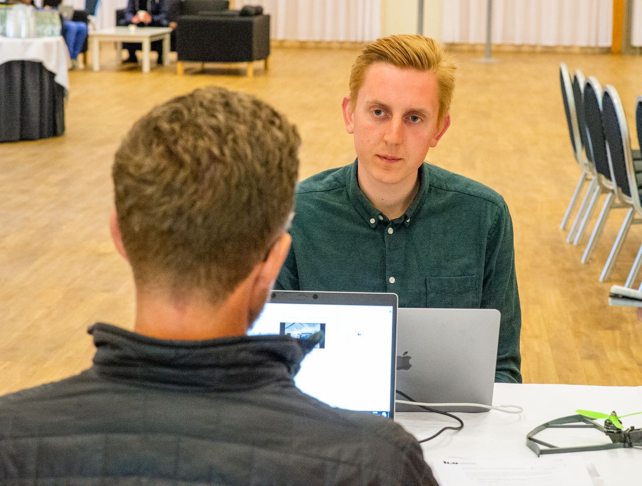 Två män sitter mitt emot varandra vid ett bord, de har sina laptops framför sig.