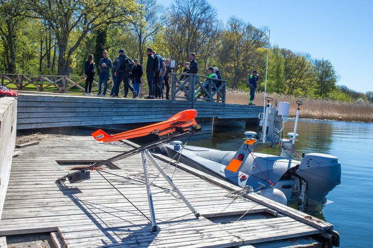 A boat at a dock. In the background there is a group of people on the dock.