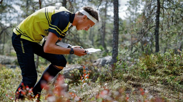 En man i träningskläder orienterar i en skog.