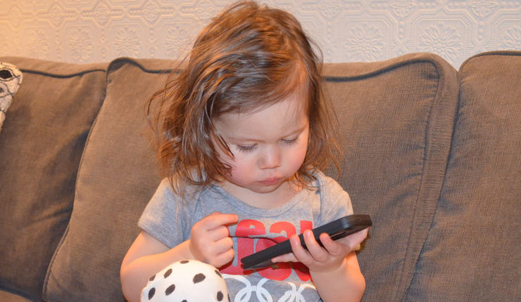 Litet barn sitter i soffa och tittar på en smartphone.