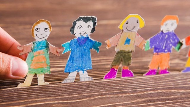 Barn gör pappersfigurer på träbakgrund.