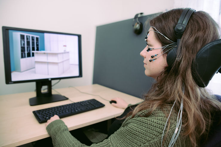 young woman with electrodes attached to her face looks at an image of an office containing a red lamp