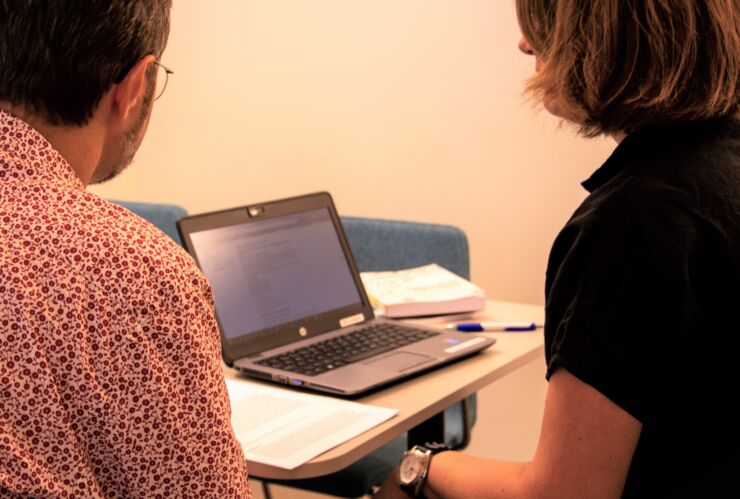 Two people at a desk with a laptop in front of them.