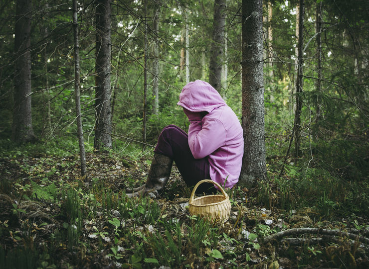 Confused person went to mushroom picking and got lost in the forest, disoriented scared and confused, northern Europe, sit under tree. Person lost in nature concept. Wearing bright colorful clothing.