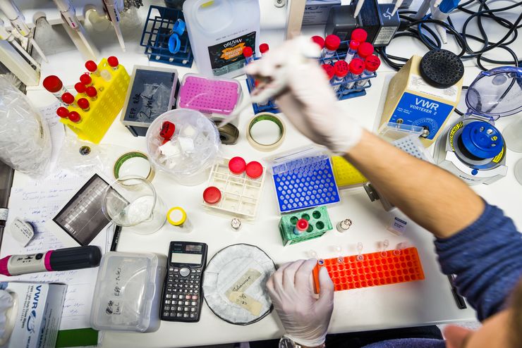 A hand with a white glove above test tubes and other equipment