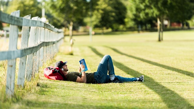 Student som studerar liggande i gräset på Campus Valla