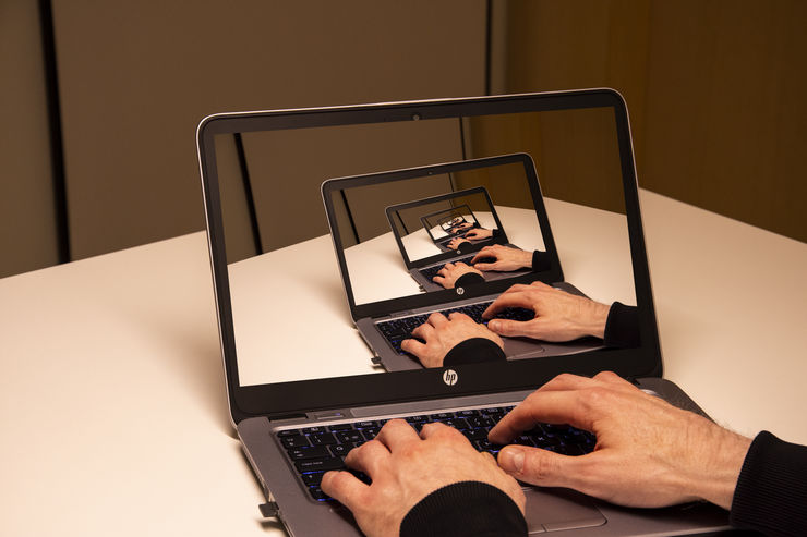 A pair of hands typing on a laptop with the same image displayed on the laptop screen in a 