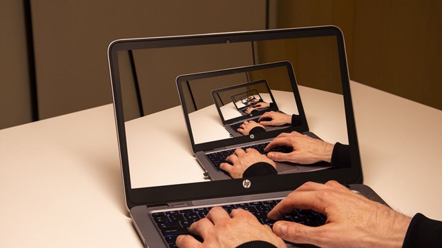 Hands writing on a laptop with the same image shown on the laptop screen.
