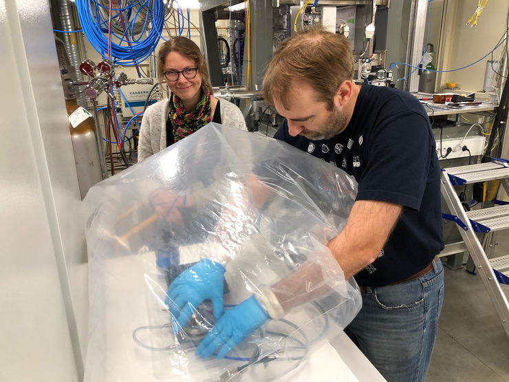 scientist works with his hands in a glove bag that protects the material sample.